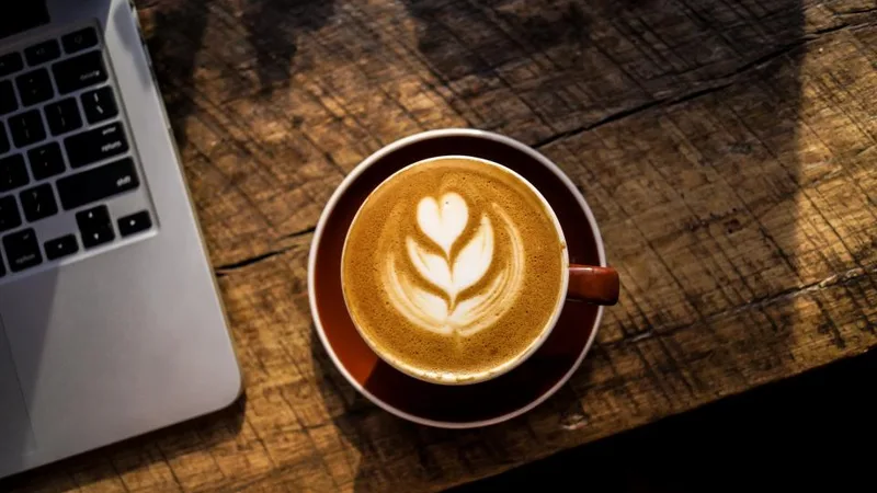 A latte with foam art next to a laptop